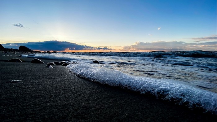 Waves crashing on a dark sand beach at sunset