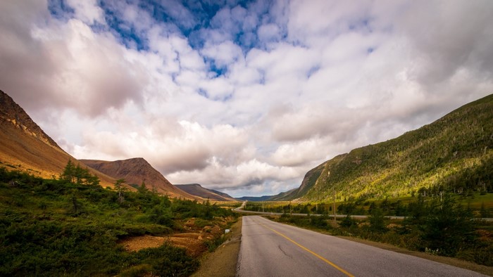 Road through a valley with mountains and clouds