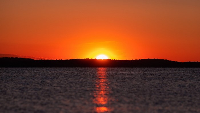 Sunset over a body of water with a silhouetted horizon
