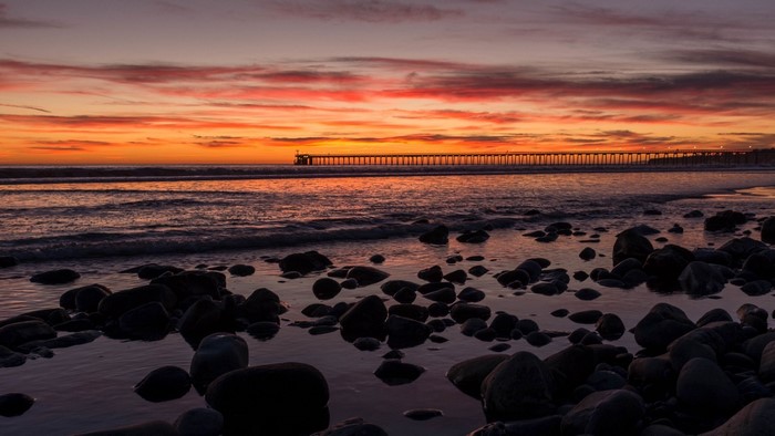 Sunset over the ocean with a pier and rocks