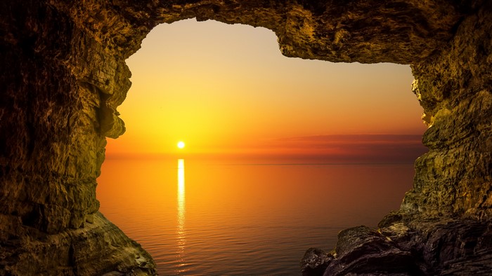 Cave entrance overlooking a 4K sunset over the ocean