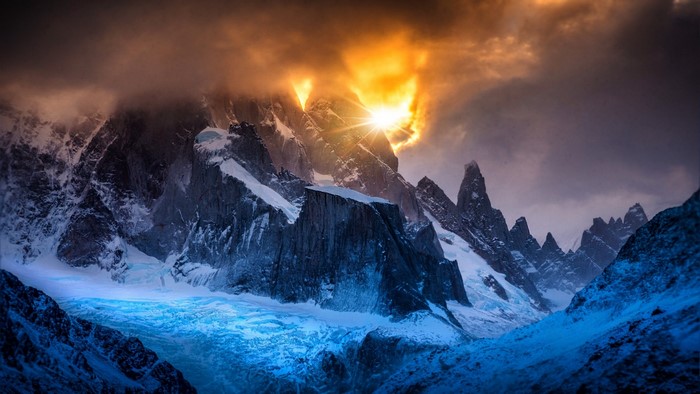 Sunlight breaking through clouds over snowy mountains