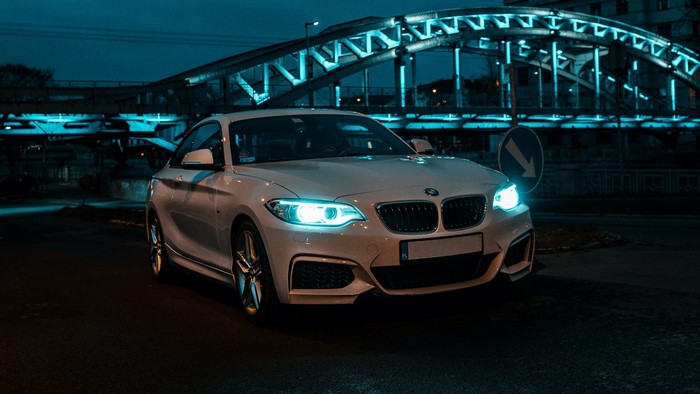 White BMW coupe parked under a blue illuminated bridge at night