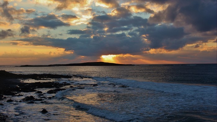 Sunset over the ocean with waves and island