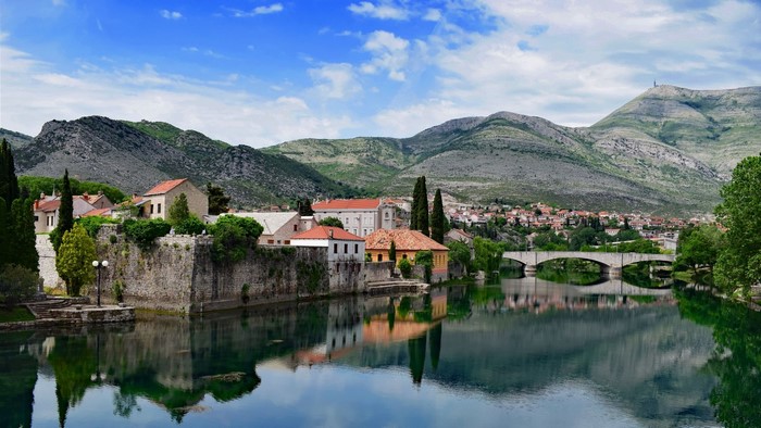 Stone buildings on a riverbank with mountains in the background