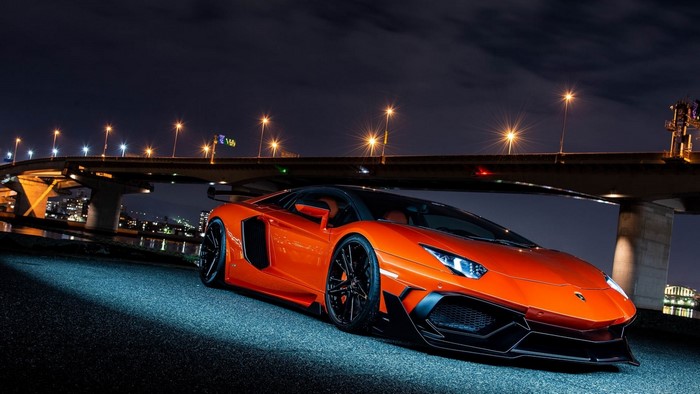 Orange Lamborghini Aventador parked under a bridge at night