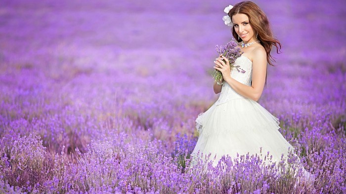 Woman in white dress holding lavender bouquet in field