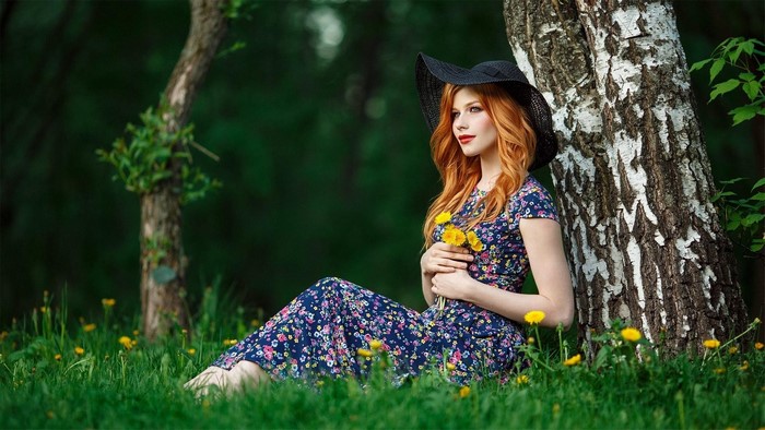 Red-haired woman in a hat and dress holding flowers
