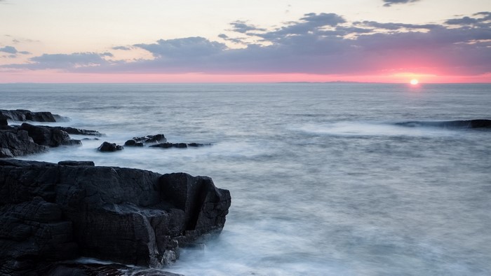 Ocean waves crashing on rocky shore at sunset