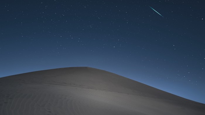 Desert dune under starry night sky with meteor