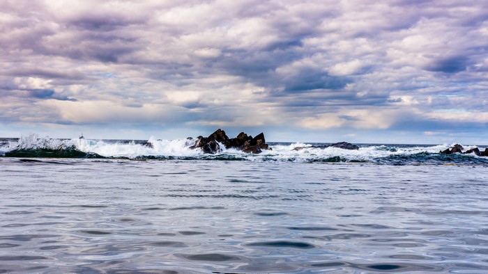 Waves crashing on rocks under cloudy sky