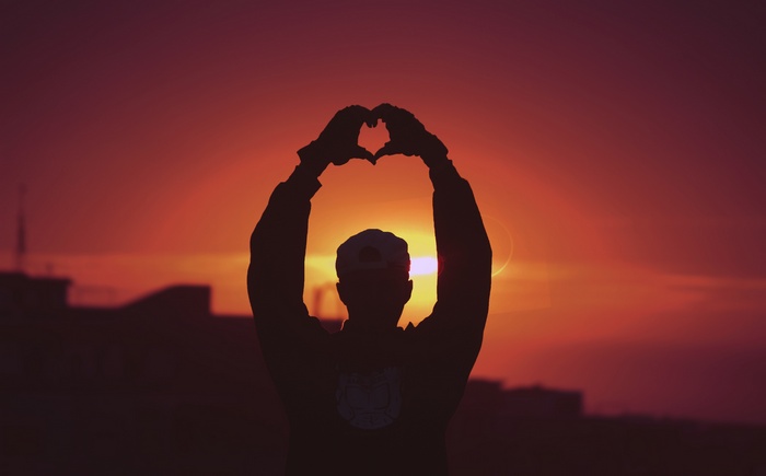 Silhouette of a person making a heart shape at sunset