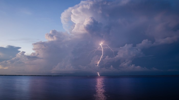 Lightning strikes over a calm body of water during a storm