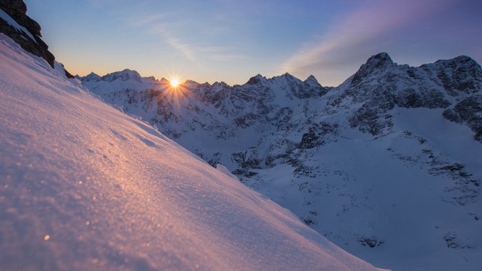 Snowy mountains at sunrise with sunburst