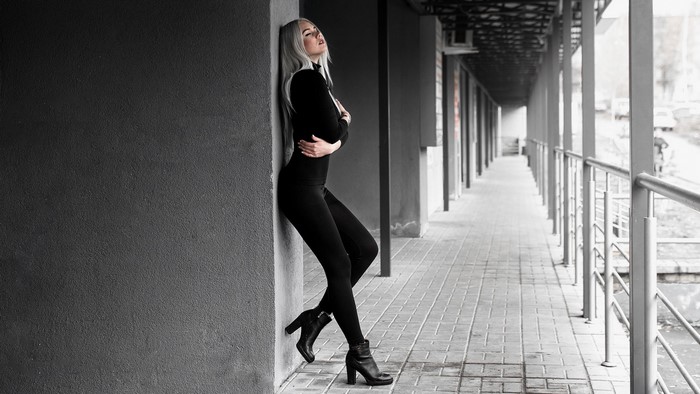 Girl in black outfit leaning against wall