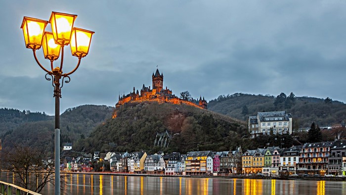 Castle on a hill overlooking a town and river at dusk
