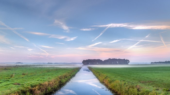 Canal through misty fields at sunrise