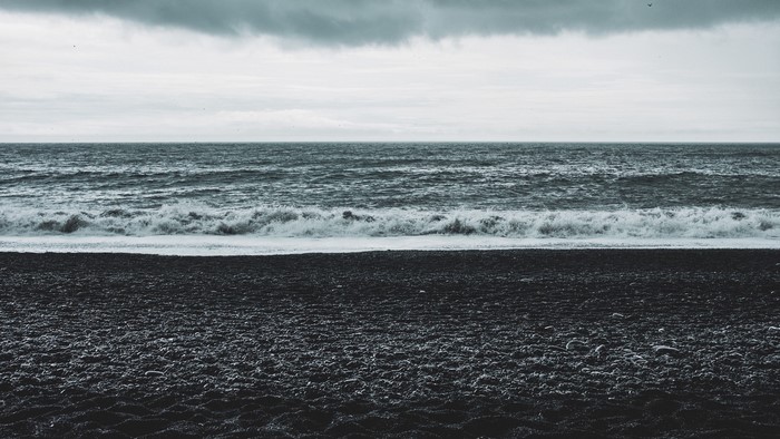 Black sand beach with waves and cloudy sky