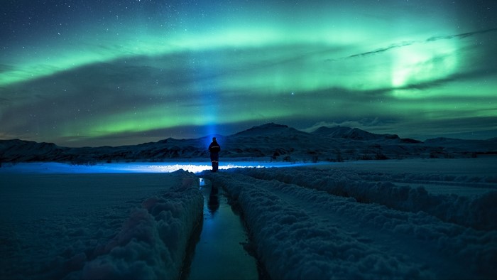 Person with flashlight under Northern Lights