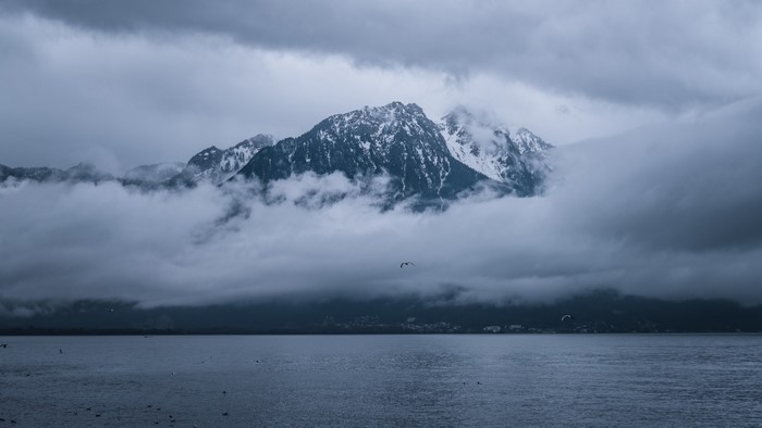 Snow-capped mountains shrouded in clouds over a lake