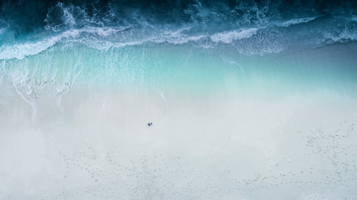 Aerial view of a beach with waves and footprints
