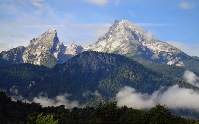 Jagged mountain peaks with green forested slopes and clouds