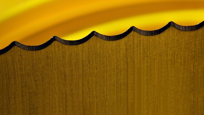 Close-up of a serrated metal blade with a yellow background