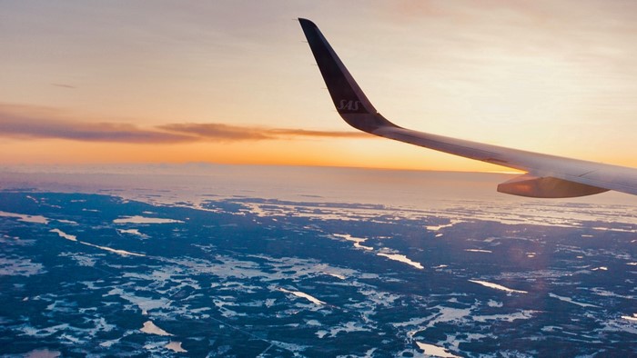 Airplane wing over frozen landscape at sunset