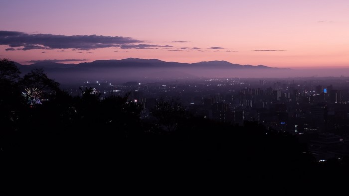 Cityscape at dusk with mountains and pinkish sky