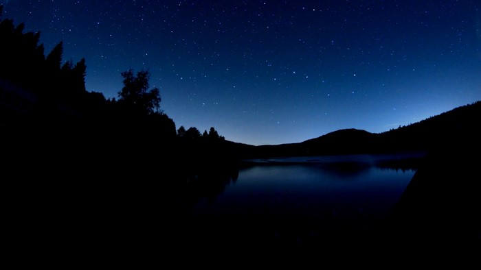 Starry Night Sky Over a Dark Lake and Forest