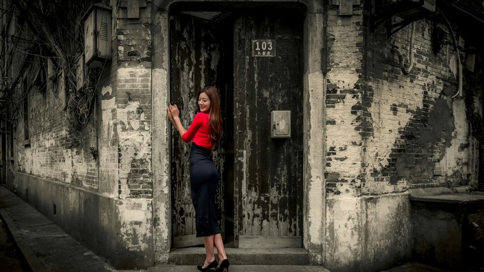 Woman in red top and black skirt by old door