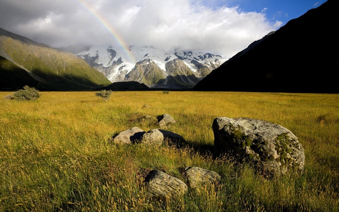 Rainbow over snowy mountains and a grassy field