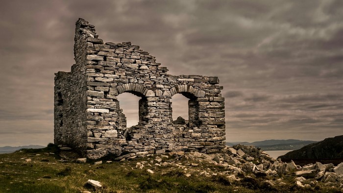 Stone ruins with arched windows on a grassy hill