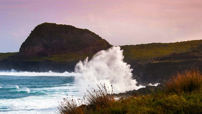 Waves crashing on a rocky coastline with a hill