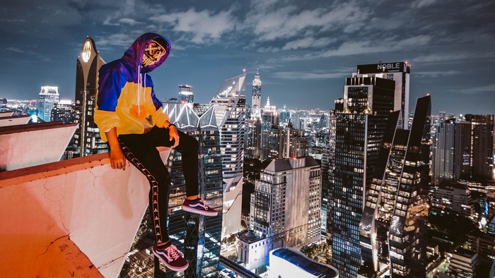 Person in mask on rooftop overlooking city at night