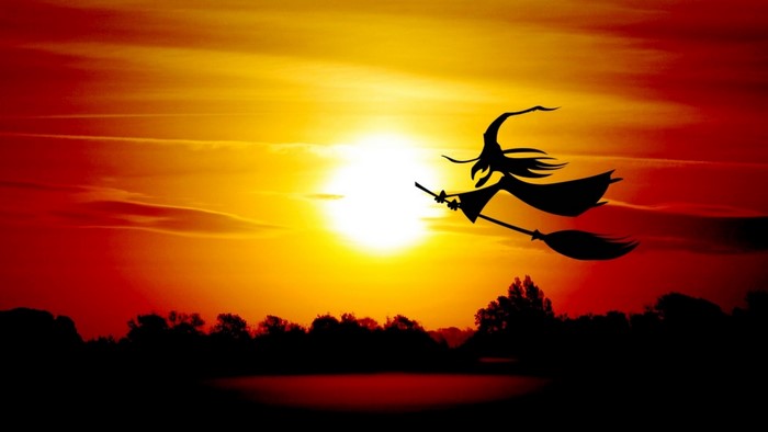 Silhouette of a witch flying on a broomstick at sunset