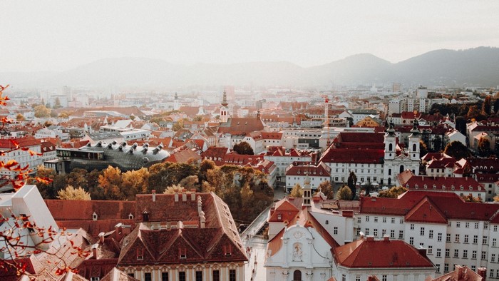 Aerial view of a European city with red-tiled roofs and mountains in the background