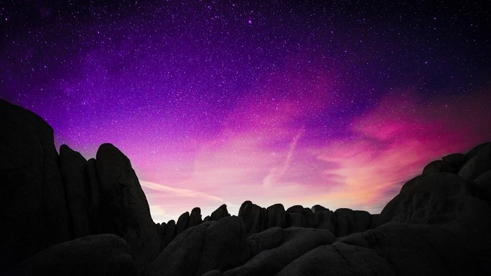 Purple and pink starry sky over dark rocks
