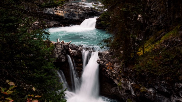 Turquoise river flowing over rocky waterfalls surrounded by dark forest