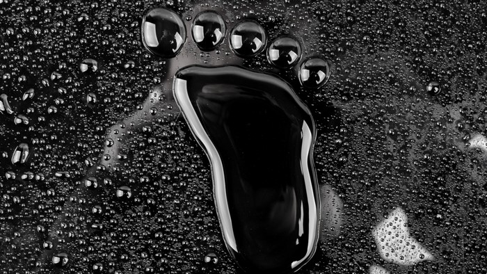 Footprint made of black liquid on a surface with water droplets