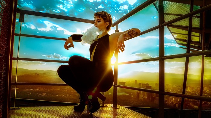 Woman exhaling smoke on a rooftop at sunset