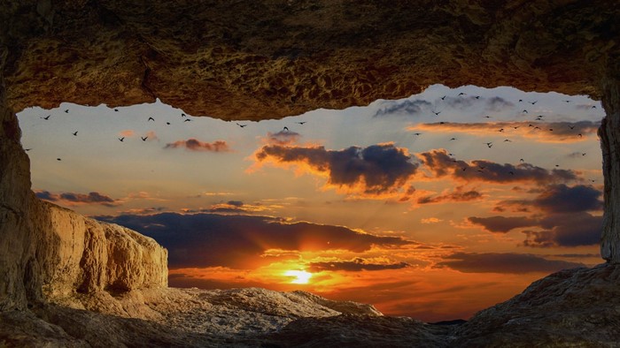 Cave opening overlooking sunset with birds