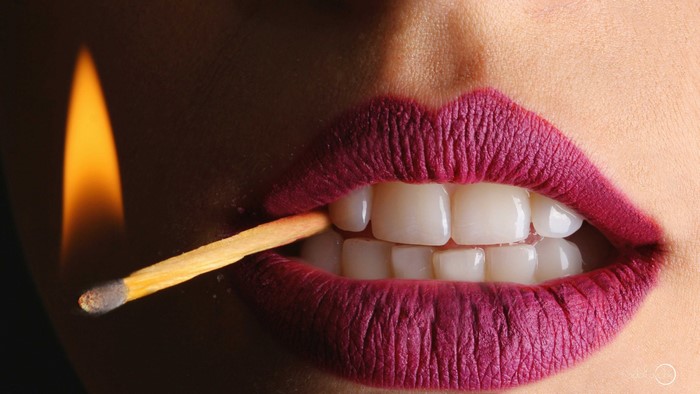 Close-up of lips holding a lit match