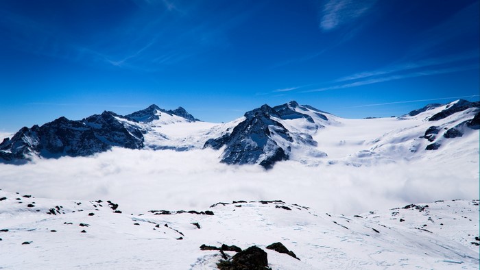 Snowy mountains above clouds under blue sky