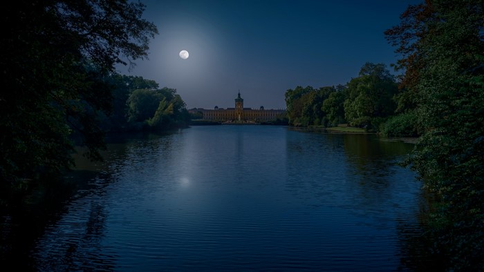 Castle by the lake under the full moon at night