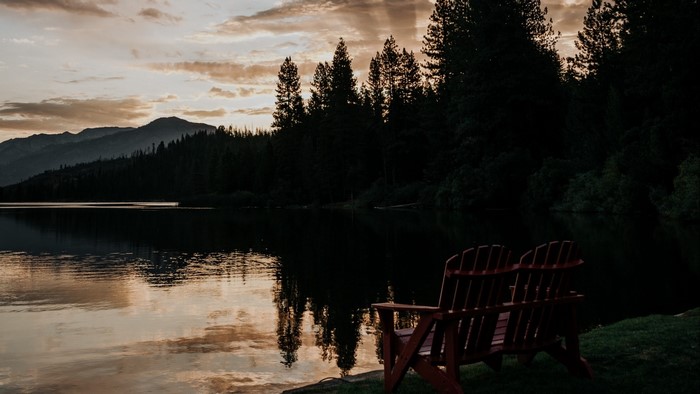 Two Adirondack chairs by a lake at sunset