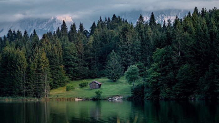 Small cabin by a lake with forest and mountains