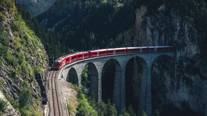Red train on a stone bridge in a mountain forest