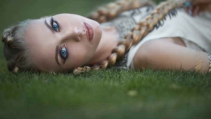 Woman with blue eyes and braids lying on grass