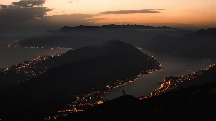 Silhouette of a person on a mountain overlooking a lake at sunset